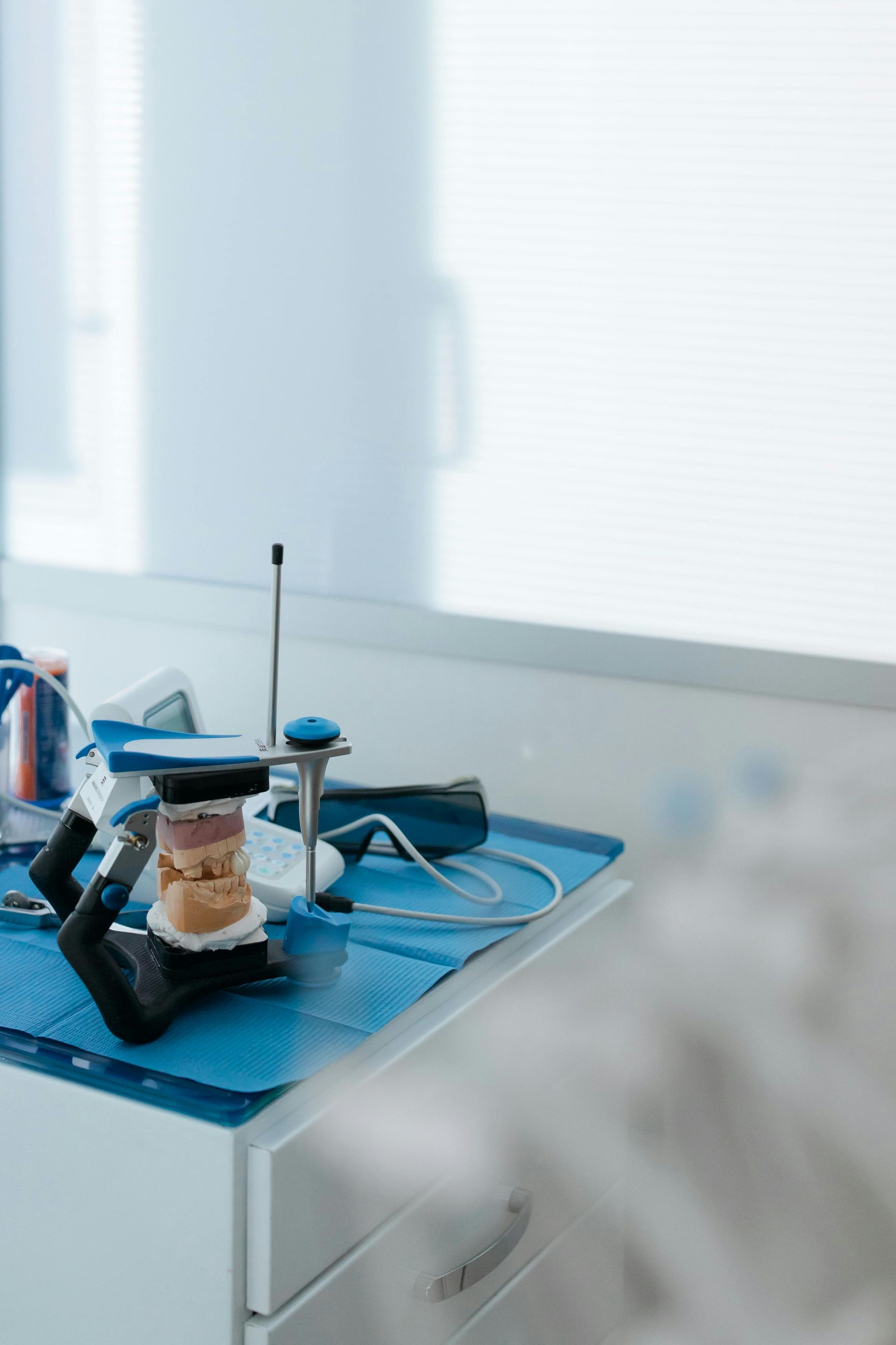 Banco da laboratorio blu con attrezzature, cavi e un piccolo vaso accanto a una finestra soleggiata