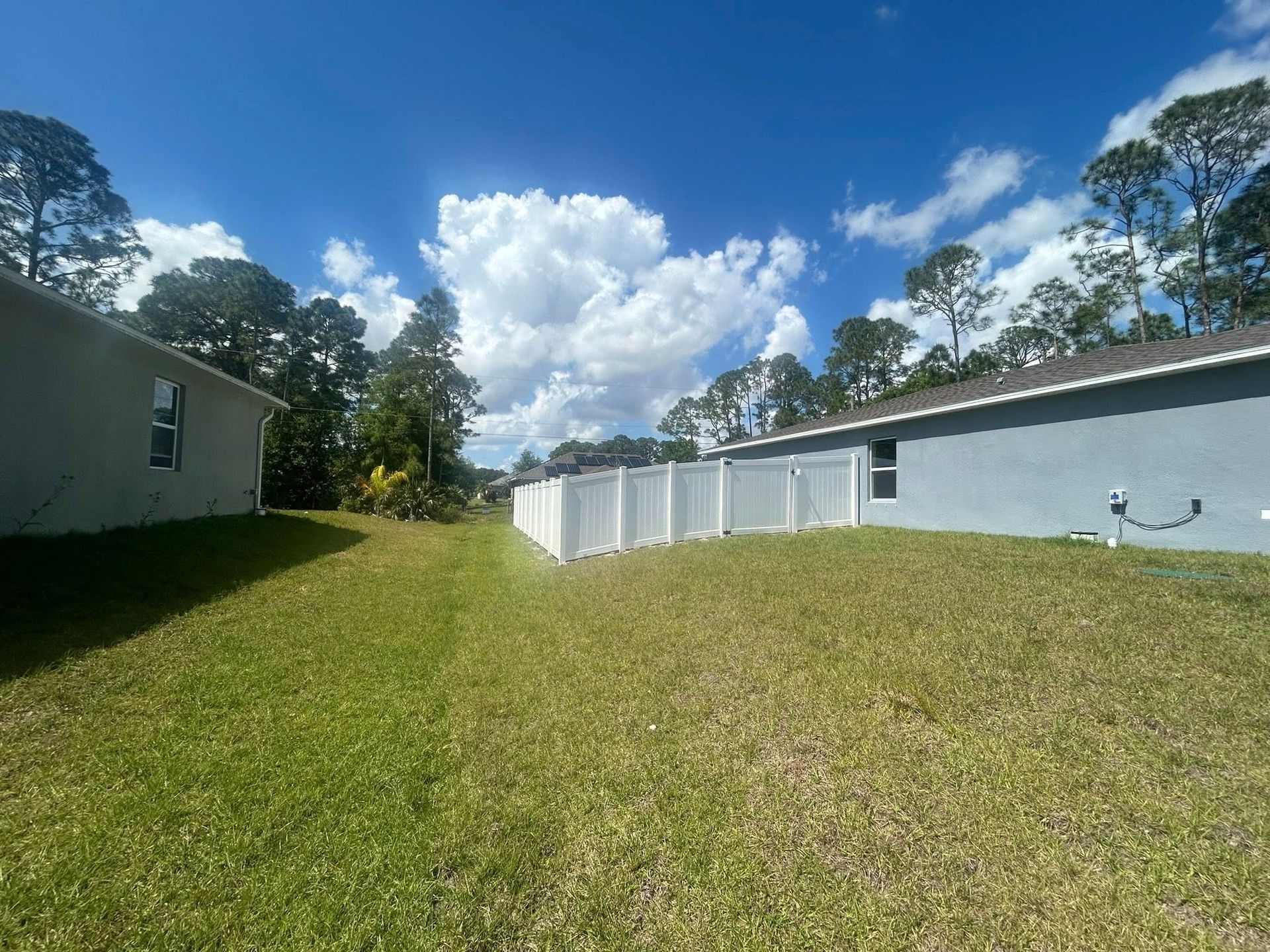 A backyard with a white fence and a house in the background.