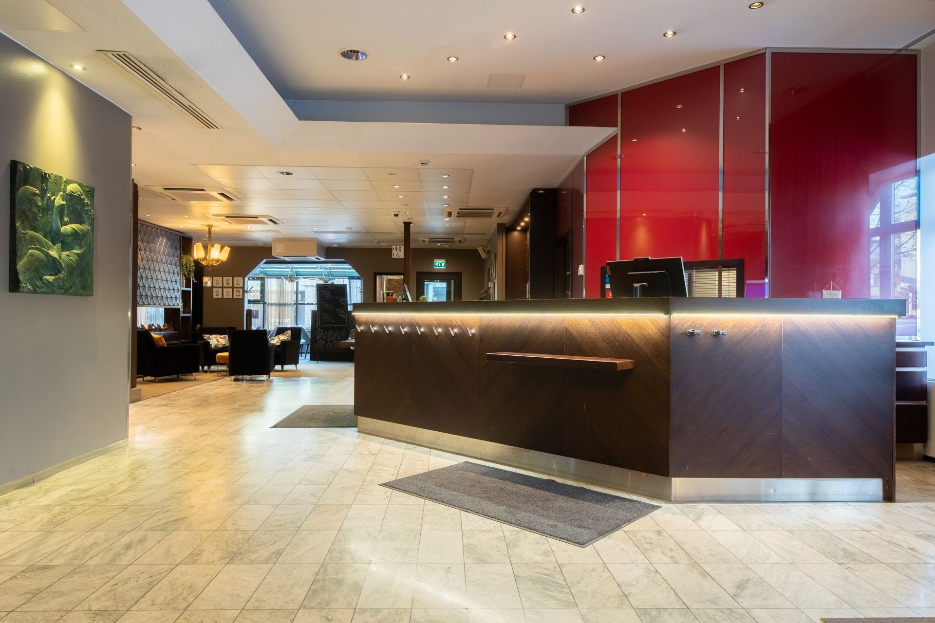 A hotel reception area with a dark wood counter, red panel wall, and marble flooring.