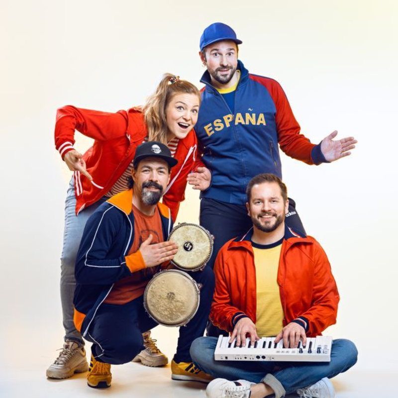 Hattu ja liivi yllään oleva henkilö istuu hymyillen vintage-pinkillä sohvalla sinivihreää, teksturoitua seinää vasten.