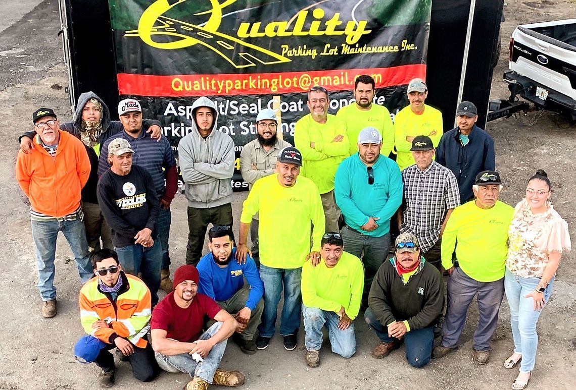 Group of people posing in front of a banner; asphalt sealing and repair team wearing safety vests.