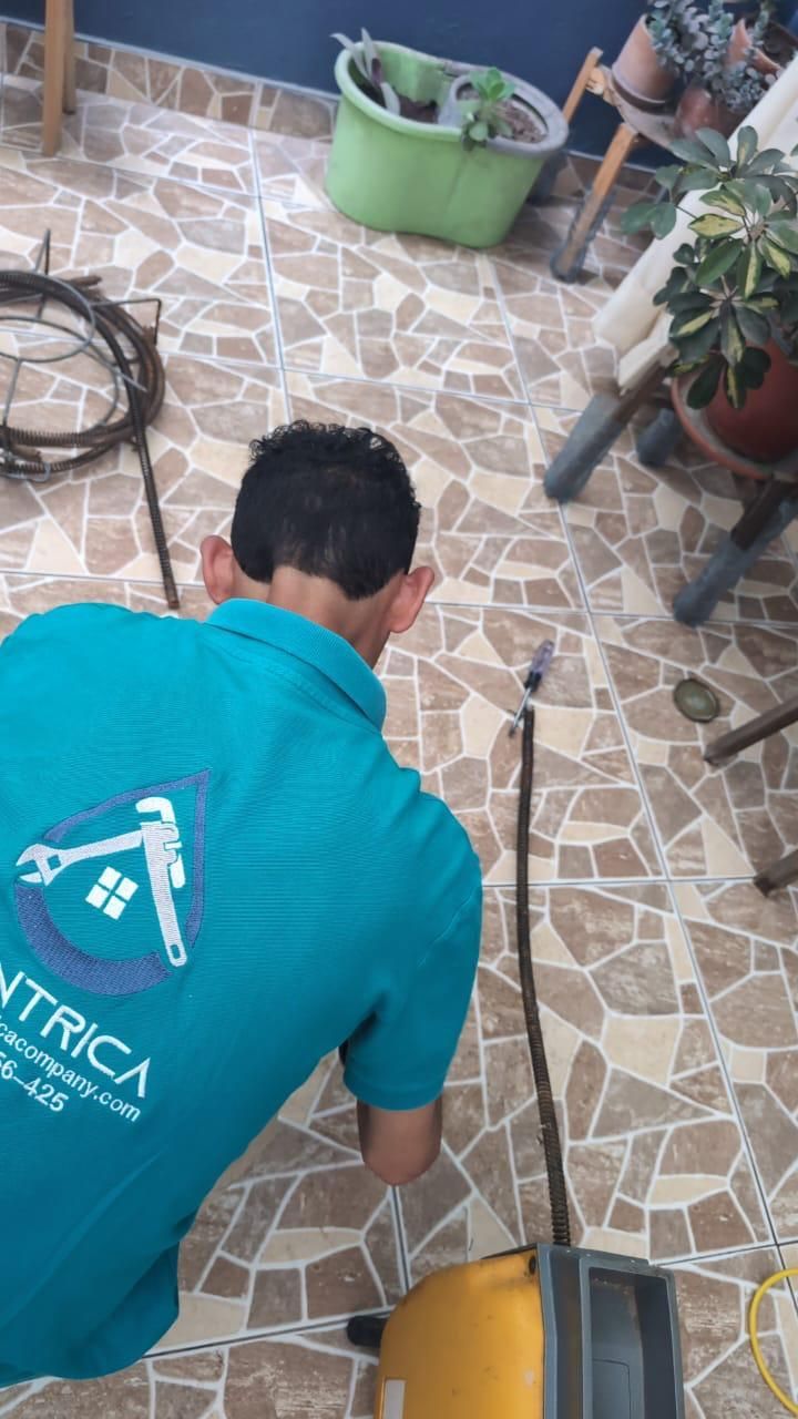 Un trabajador con camisa color turquesa está arrodillado sobre un suelo de baldosas, limpiando