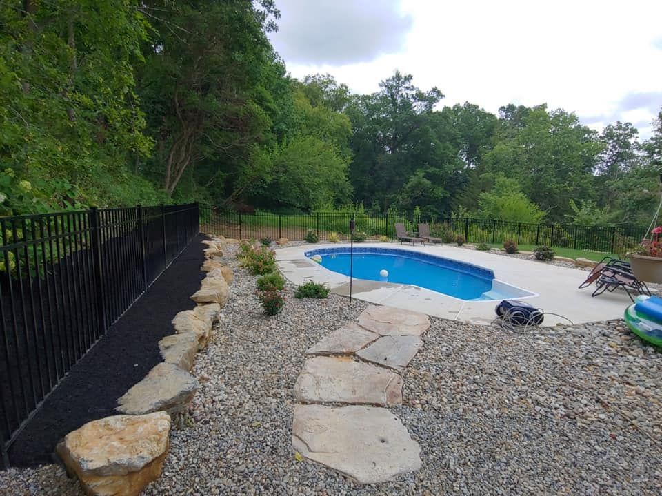 a large swimming pool is surrounded by a black fence and rocks .