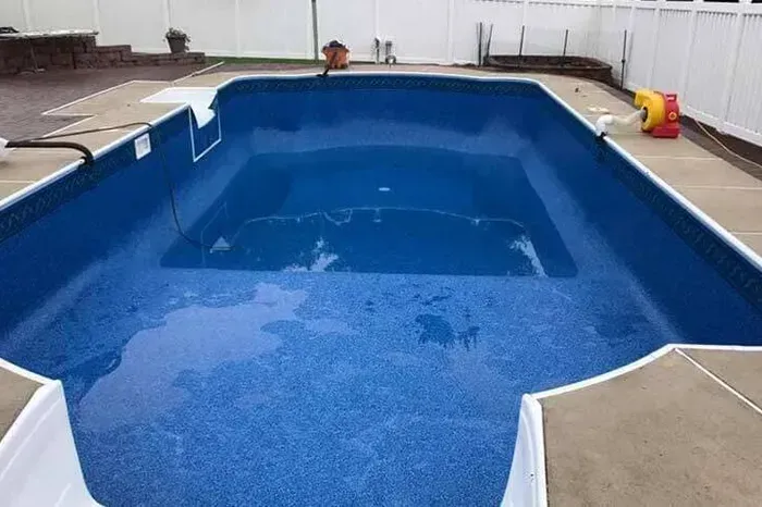 a large blue swimming pool with a white fence in the background .