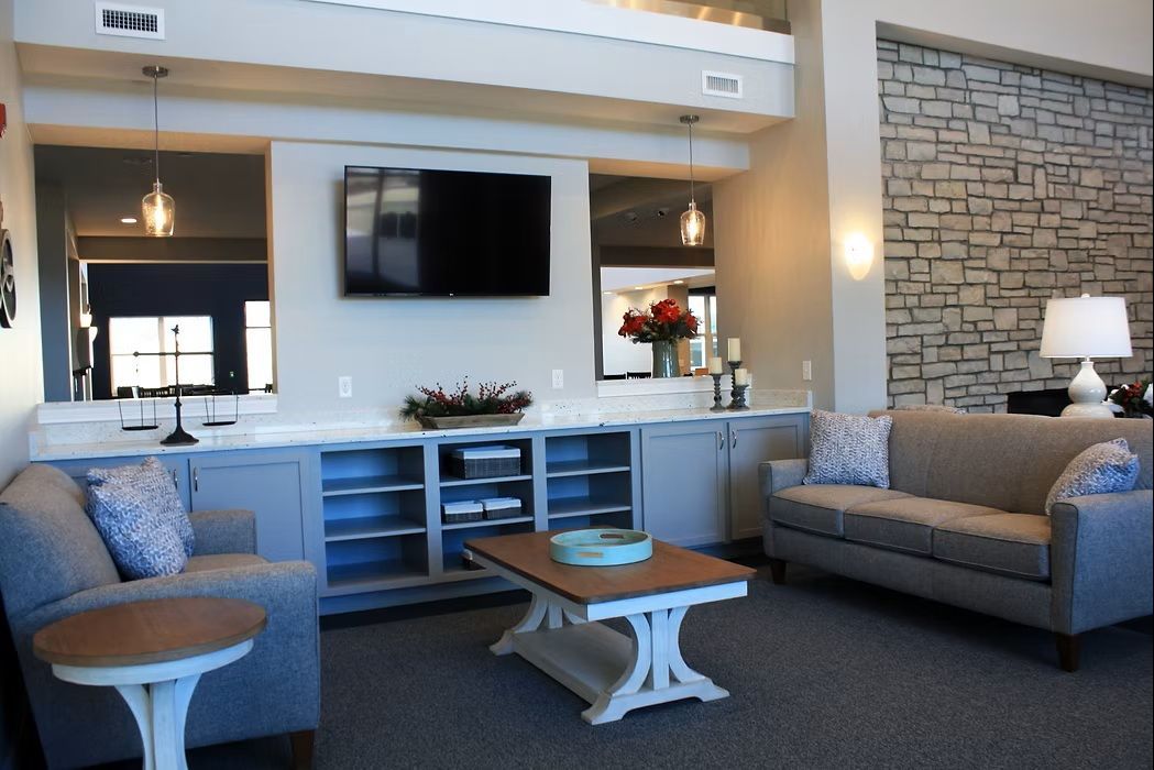 Modern living room with gray sofas, wall-mounted TV, stone accent wall, and coffee tables