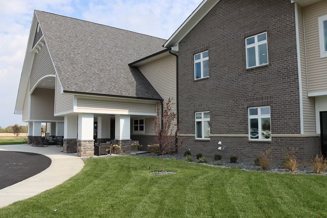 Brick building entrance with arched roof, white columns, and a curved walkway beside green lawn