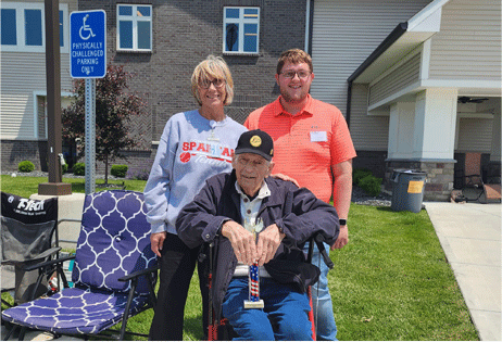 Three people posing outdoors beside an accessible parking sign and wheelchair-accessible vehicle seat.