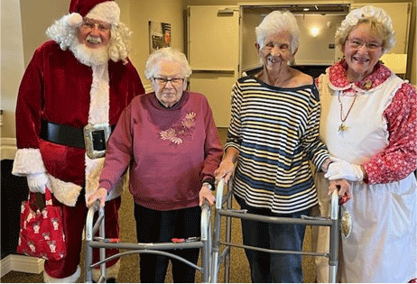 Four people in festive costumes pose indoors beside a walker and rollator.