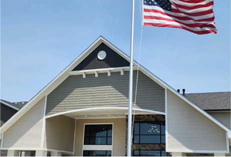 Building entrance with a large American flag flying in front under a blue sky
