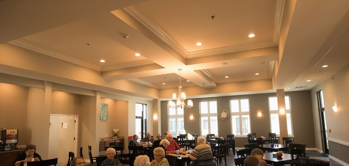 Dining hall with tables, chairs, and warm pendant lights under a high, coffered ceiling