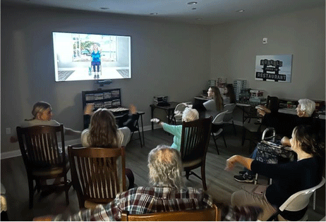 Audience seated in a dim room watching a video projected on the wall