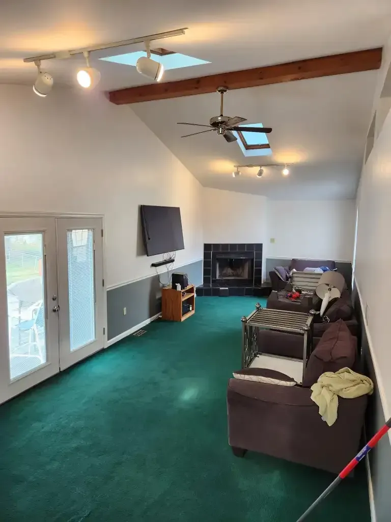 Spacious living room with green carpet, a fireplace, and a large TV. Includes brown furniture and a skylight. Spacious living room with green carpet, a fireplace, and a large TV. Includes brown furniture and a skylight.