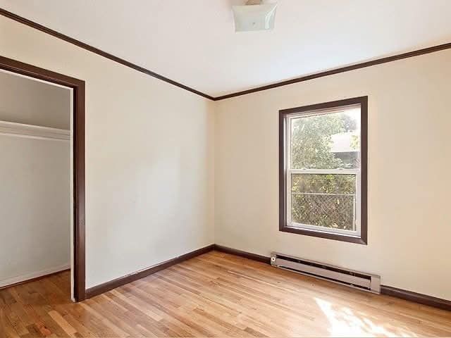 Empty room with tan walls, brown trim, hardwood floor, window, and closet. Empty room with tan walls, brown trim, hardwood floor, window, and closet.