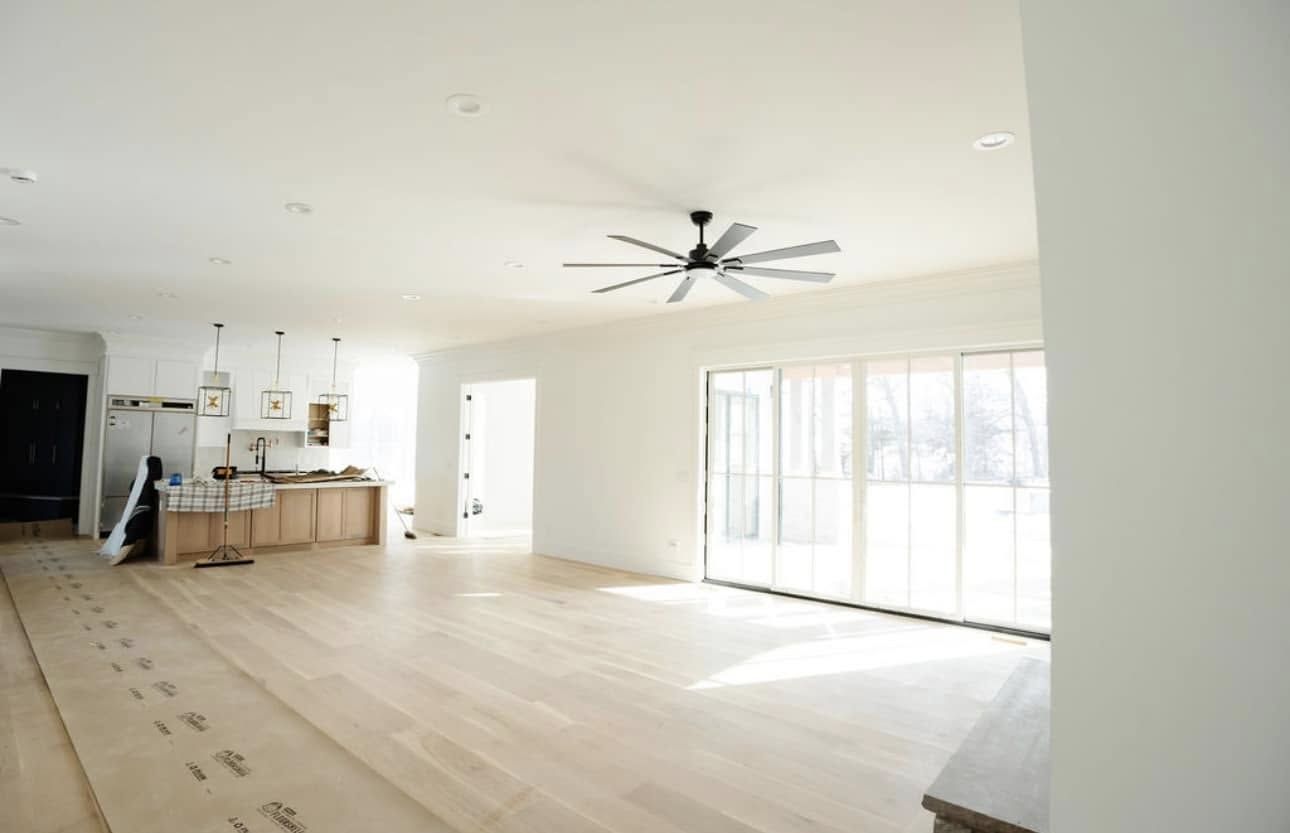 Bright, empty living space with light wood floors, white walls, and a large ceiling fan. Bright, empty living space with light wood floors, white walls, and a large ceiling fan.