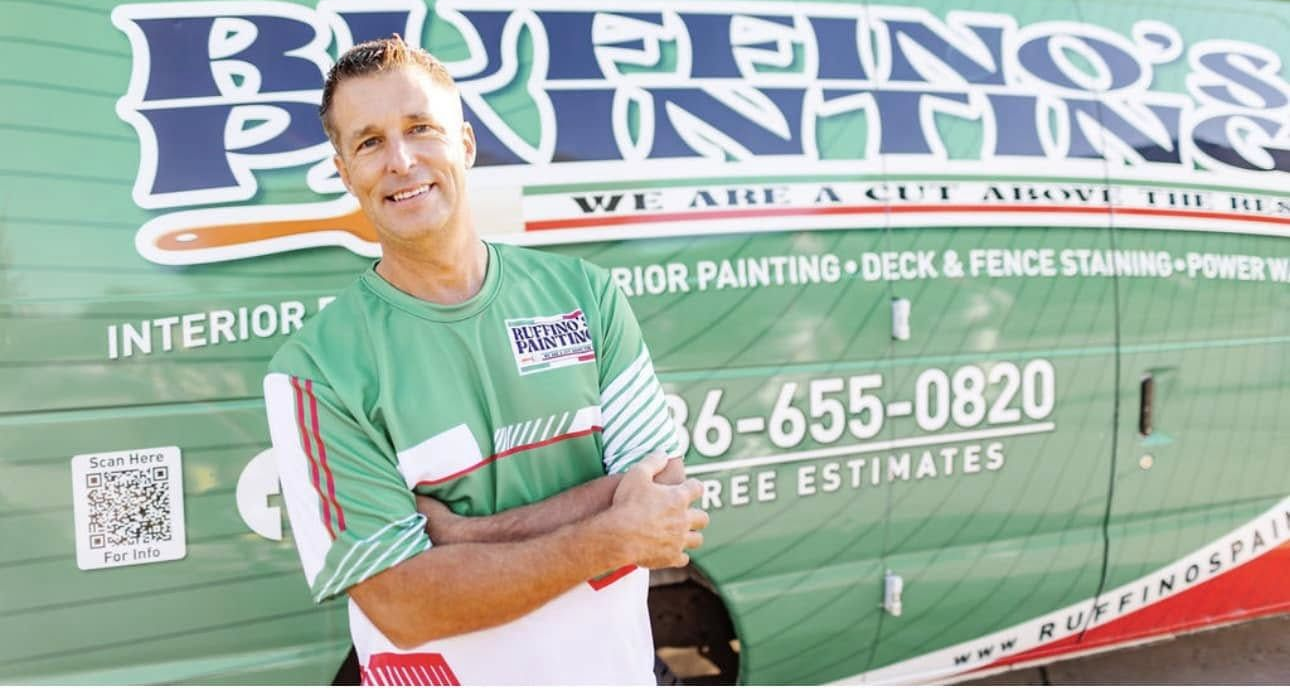 Man with arms crossed smiles in front of green and white 