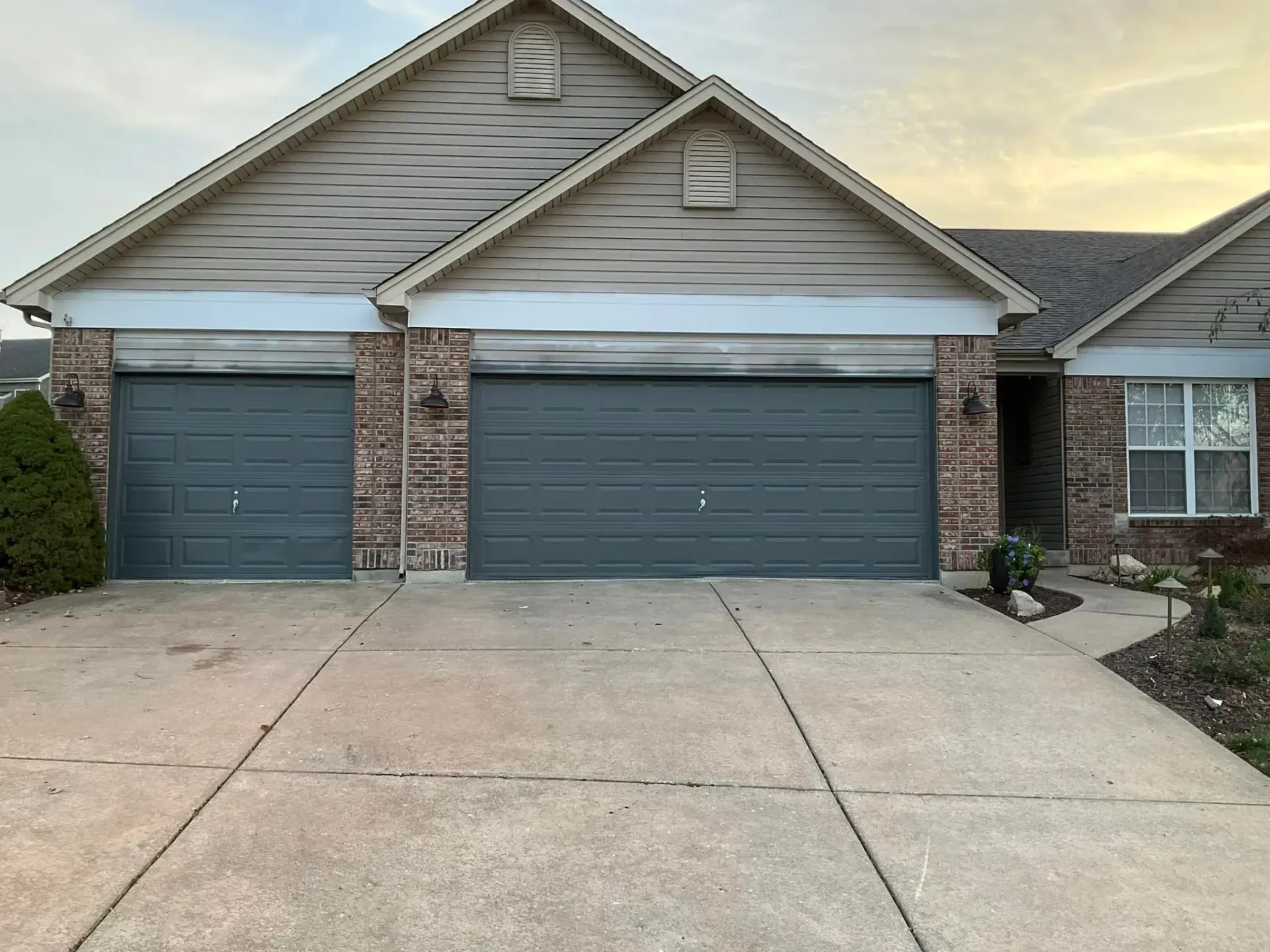 Two-car garage with gray doors on a tan house with a concrete driveway.
