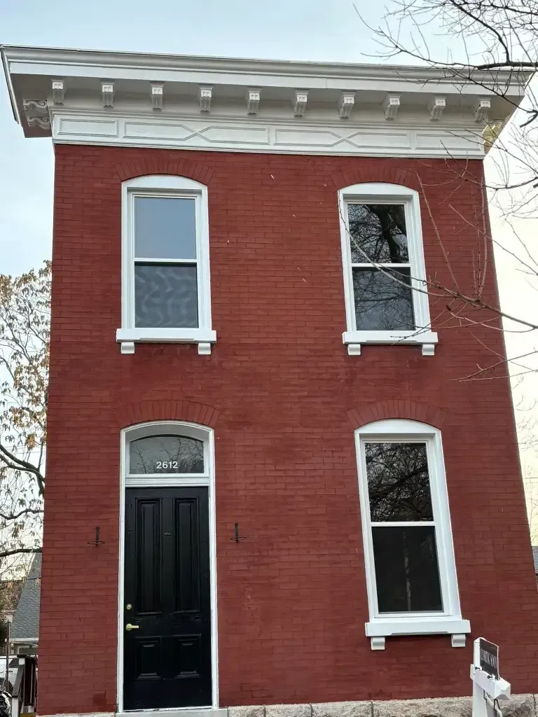 Red brick two-story house with white trim around windows and decorative cornice. Black front door. Red brick two-story house with white trim around windows and decorative cornice. Black front door.