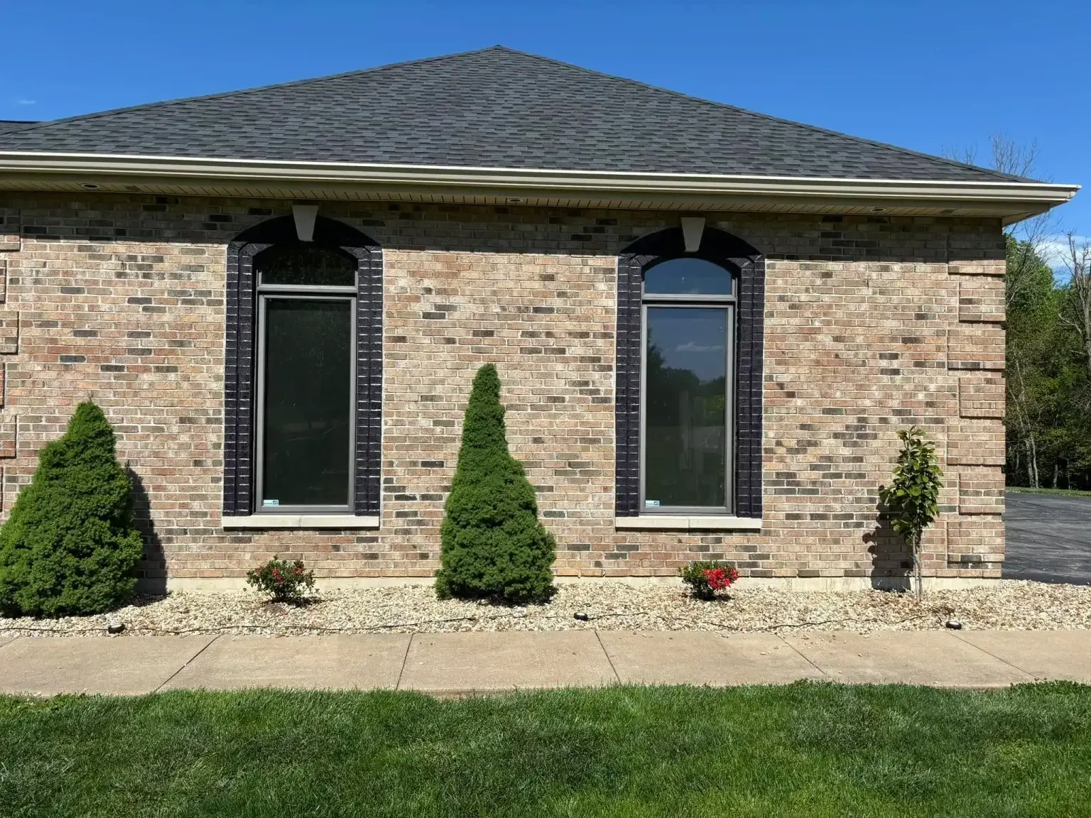 Brick house with two arched windows, black shutters, and green landscaping. Brick house with two arched windows, black shutters, and green landscaping.