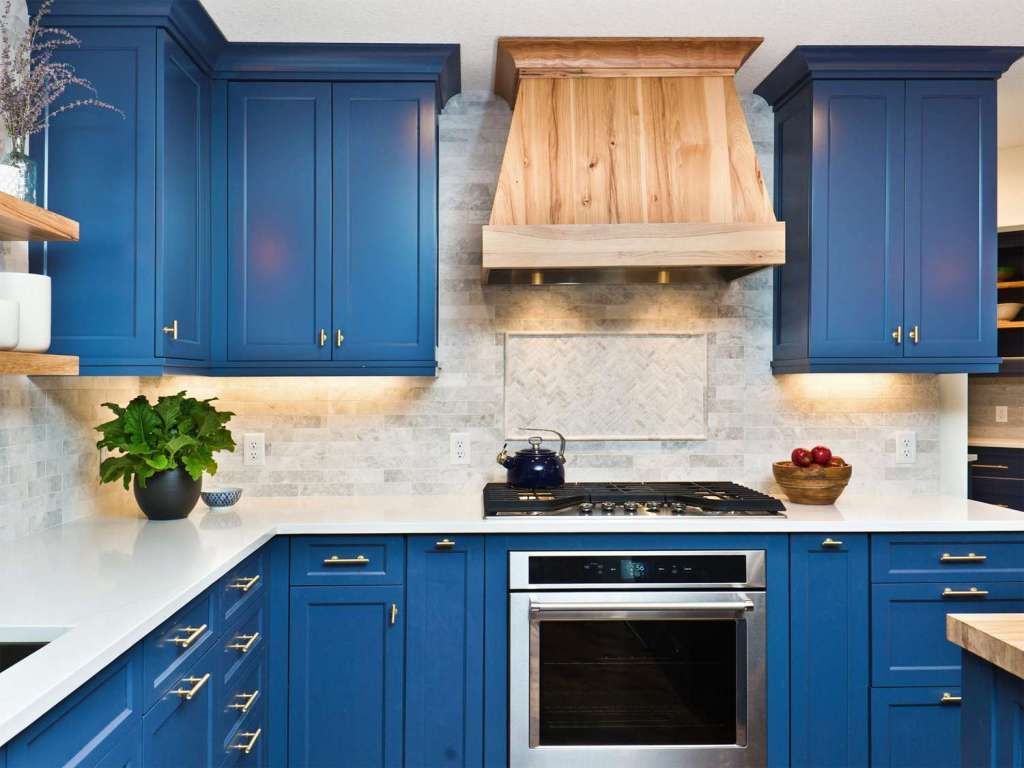 Blue kitchen cabinets with white countertops, wooden range hood, and stainless steel oven. Blue kitchen cabinets with white countertops, wooden range hood, and stainless steel oven.