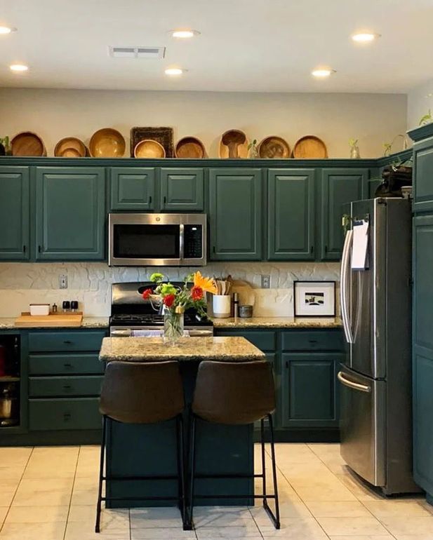 Dark teal kitchen with island and stainless steel appliances; plates on cabinets.