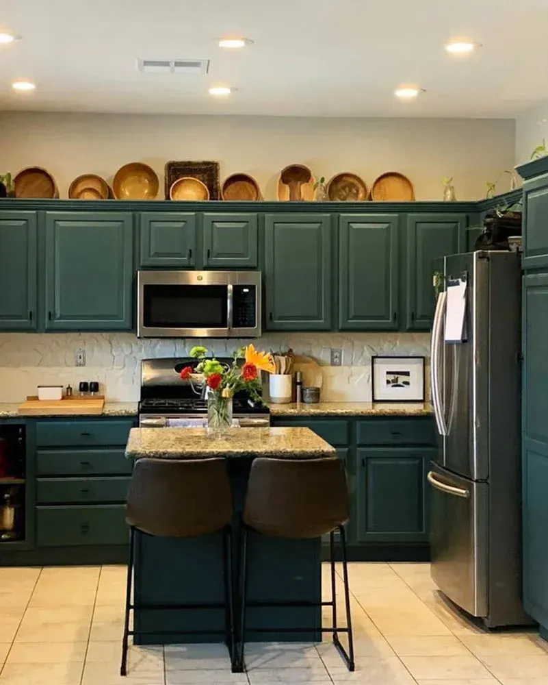 Dark teal kitchen with island and stainless steel appliances. Dishes sit above cabinets. Dark teal kitchen with island and stainless steel appliances. Dishes sit above cabinets.
