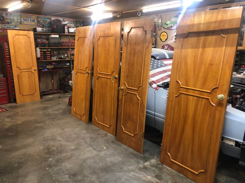 Five stained wooden doors leaning in a garage, against a car with an American flag.