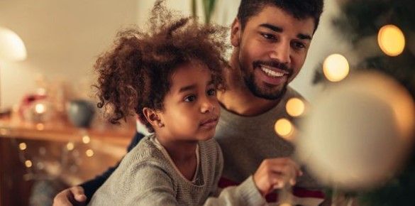 A father and child decorate a Christmas tree together. The father smiles, and the child looks intently. A father and child decorate a Christmas tree together. The father smiles, and the child looks intently.