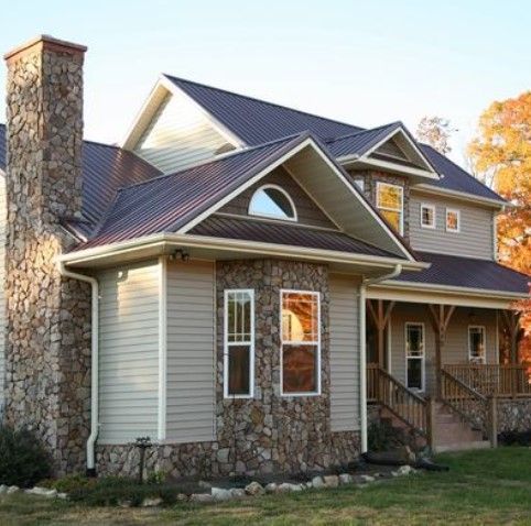 Two-story house with stone accents, tan siding, brown roof, and chimney. Sunlight reflects in windows. Two-story house with stone accents, tan siding, brown roof, and chimney. Sunlight reflects in windows.