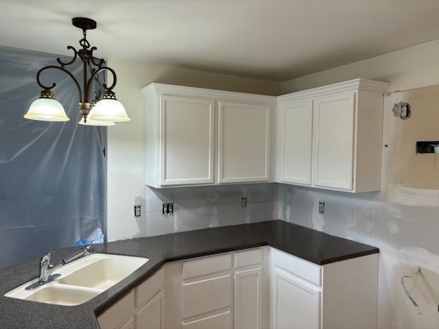 White kitchen cabinets with black countertop; a sink and a chandelier are visible. White kitchen cabinets with black countertop; a sink and a chandelier are visible.