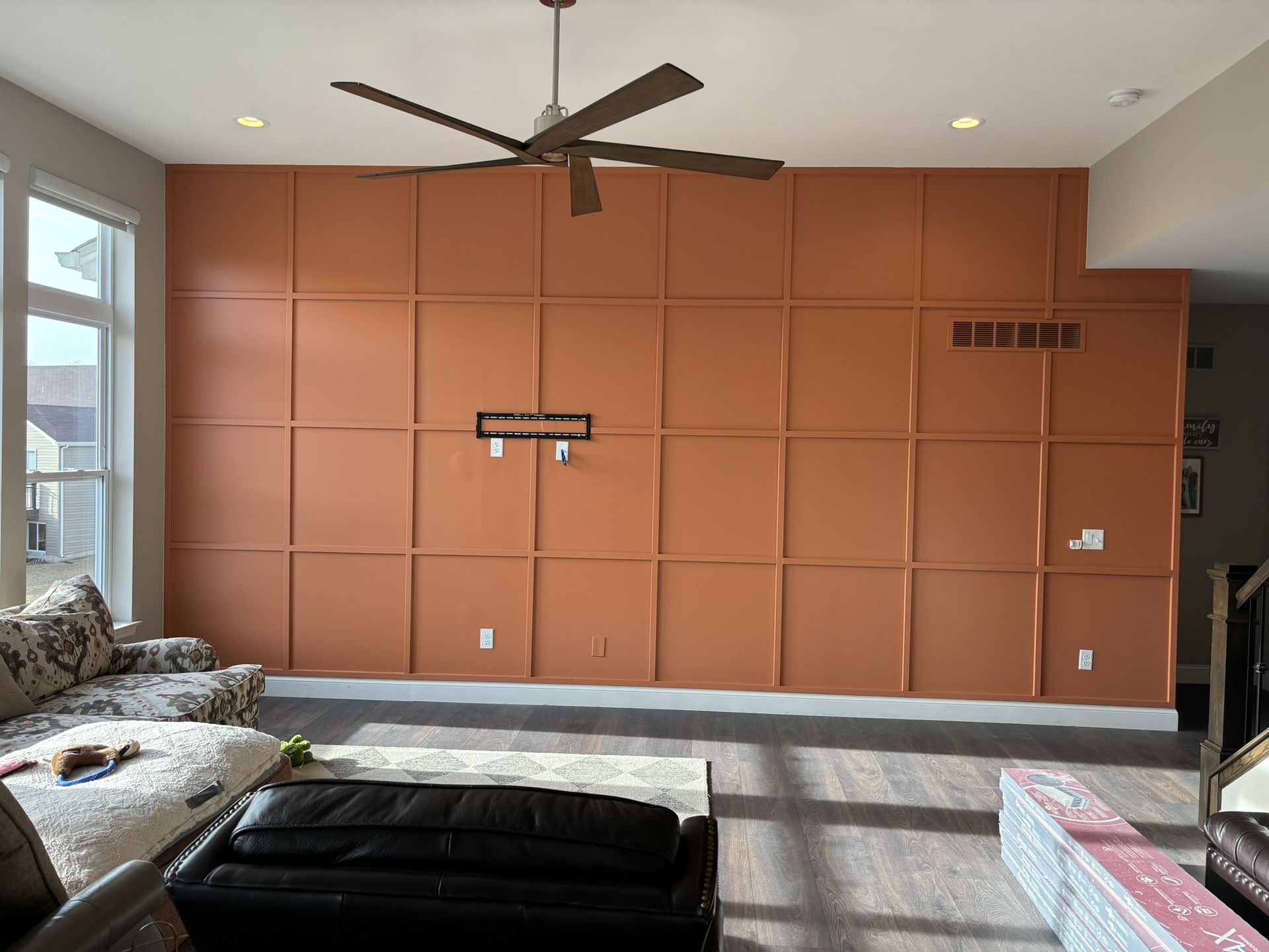 Living room with orange paneled accent wall, a couch, a ceiling fan, and a rug.