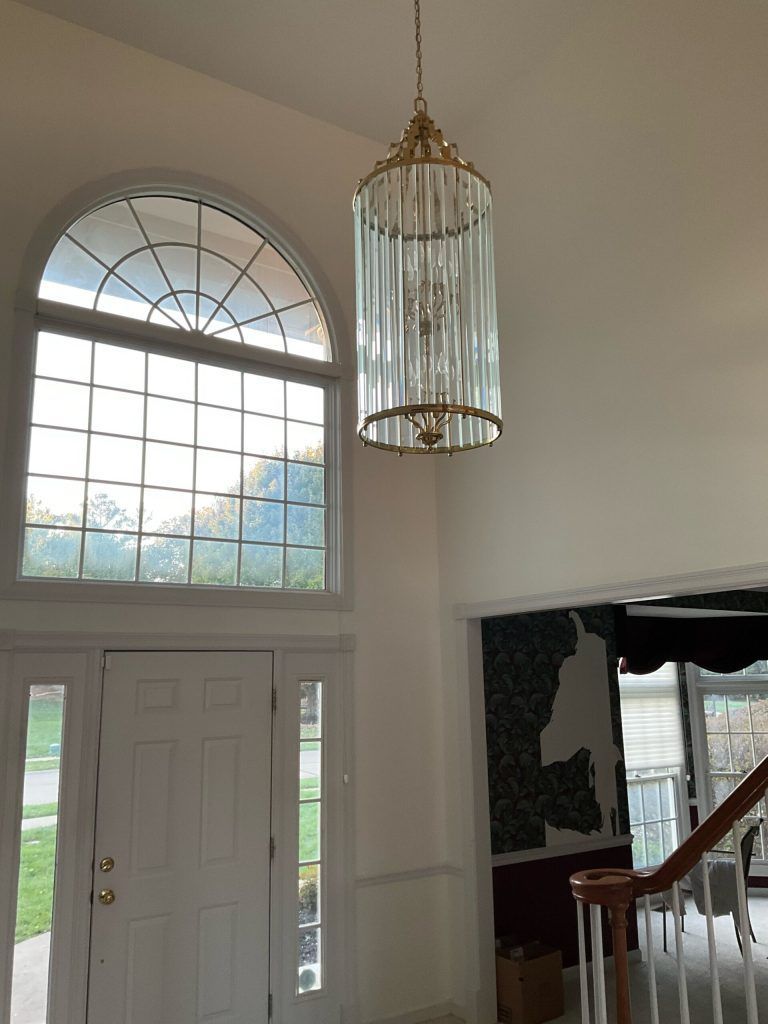 Entryway with a tall window, front door, and a chandelier. White walls and stairs. Entryway with a tall window, front door, and a chandelier. White walls and stairs.