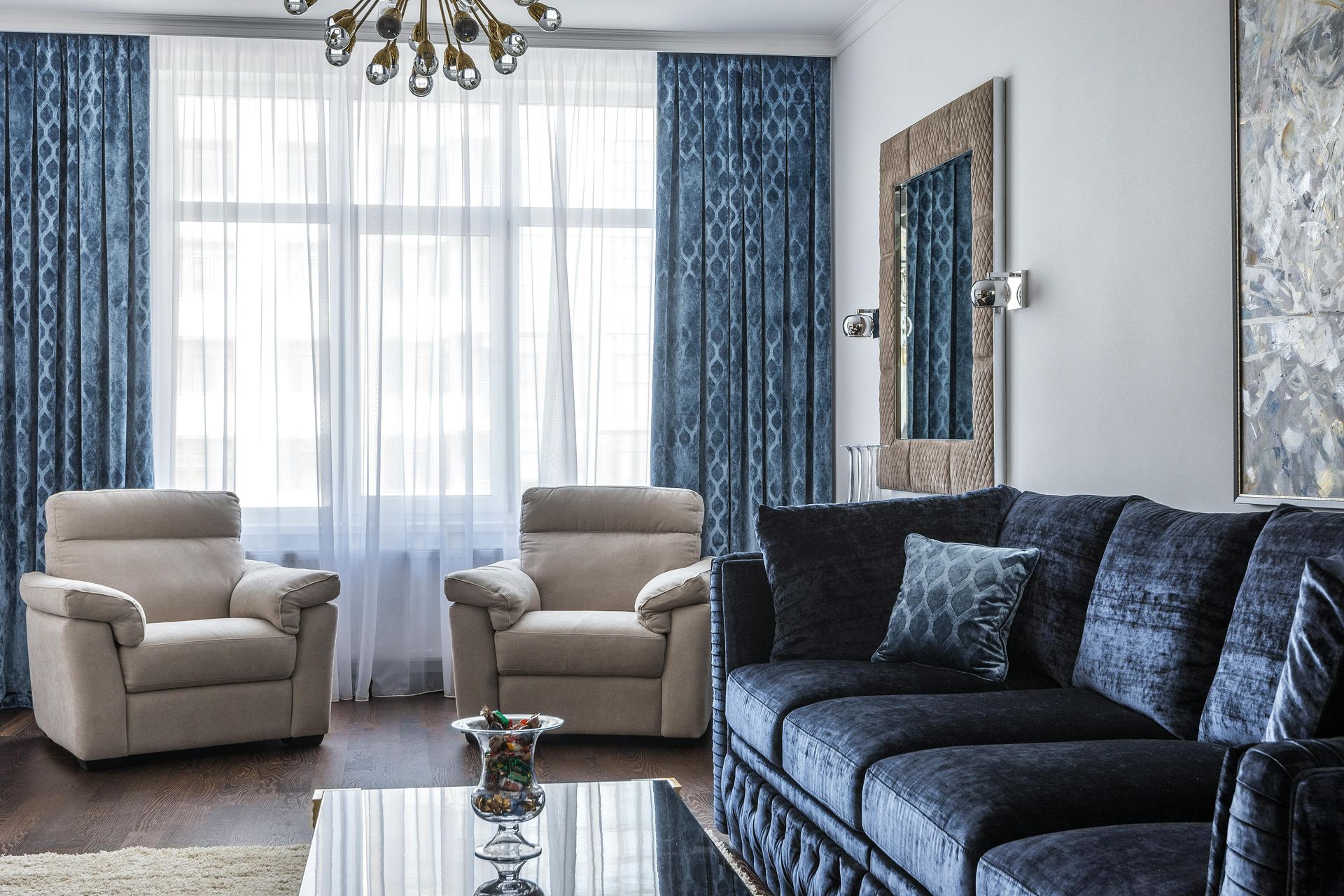 Living room with blue patterned curtains, beige armchairs, and a dark blue sectional sofa.