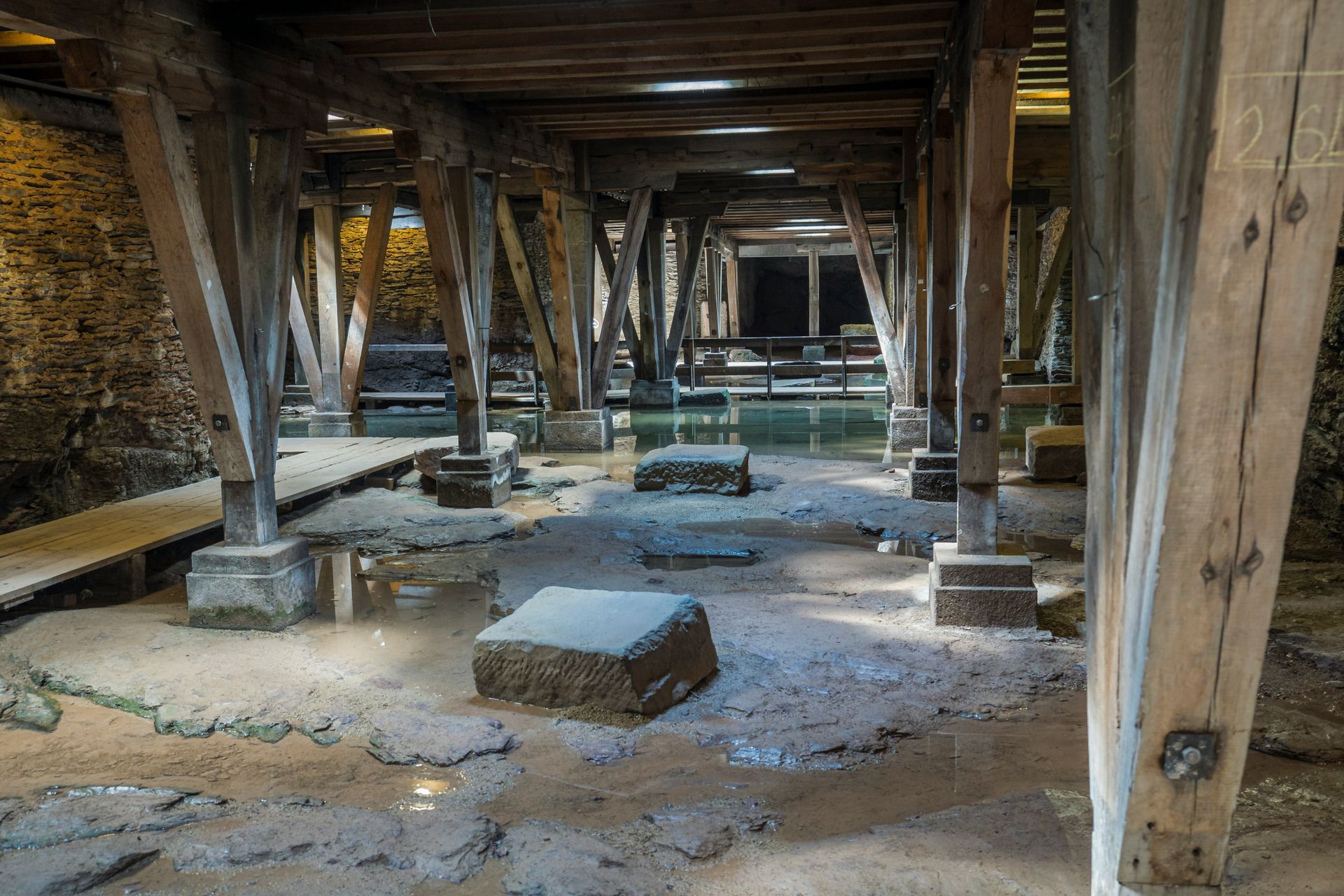 Wooden timber supports in an old underfloor crawlspace with stone blocks and dirt floor