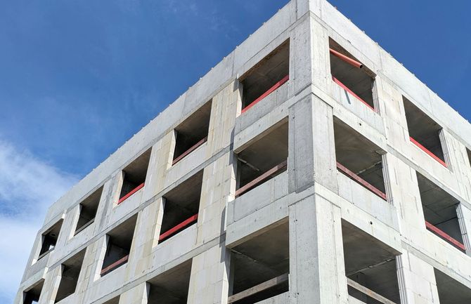 Partially constructed concrete building with open floors and red safety netting against a blue sky