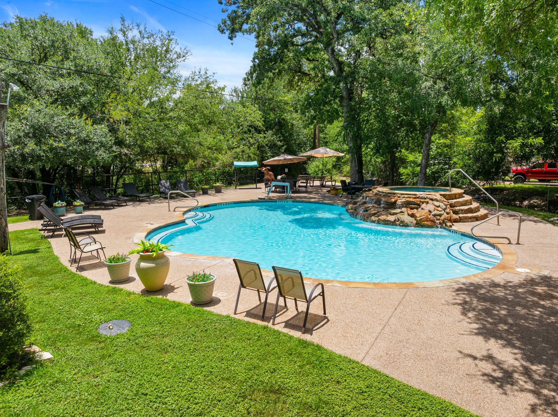 Backyard pool with lounge chairs, green lawn, and trees on a sunny day