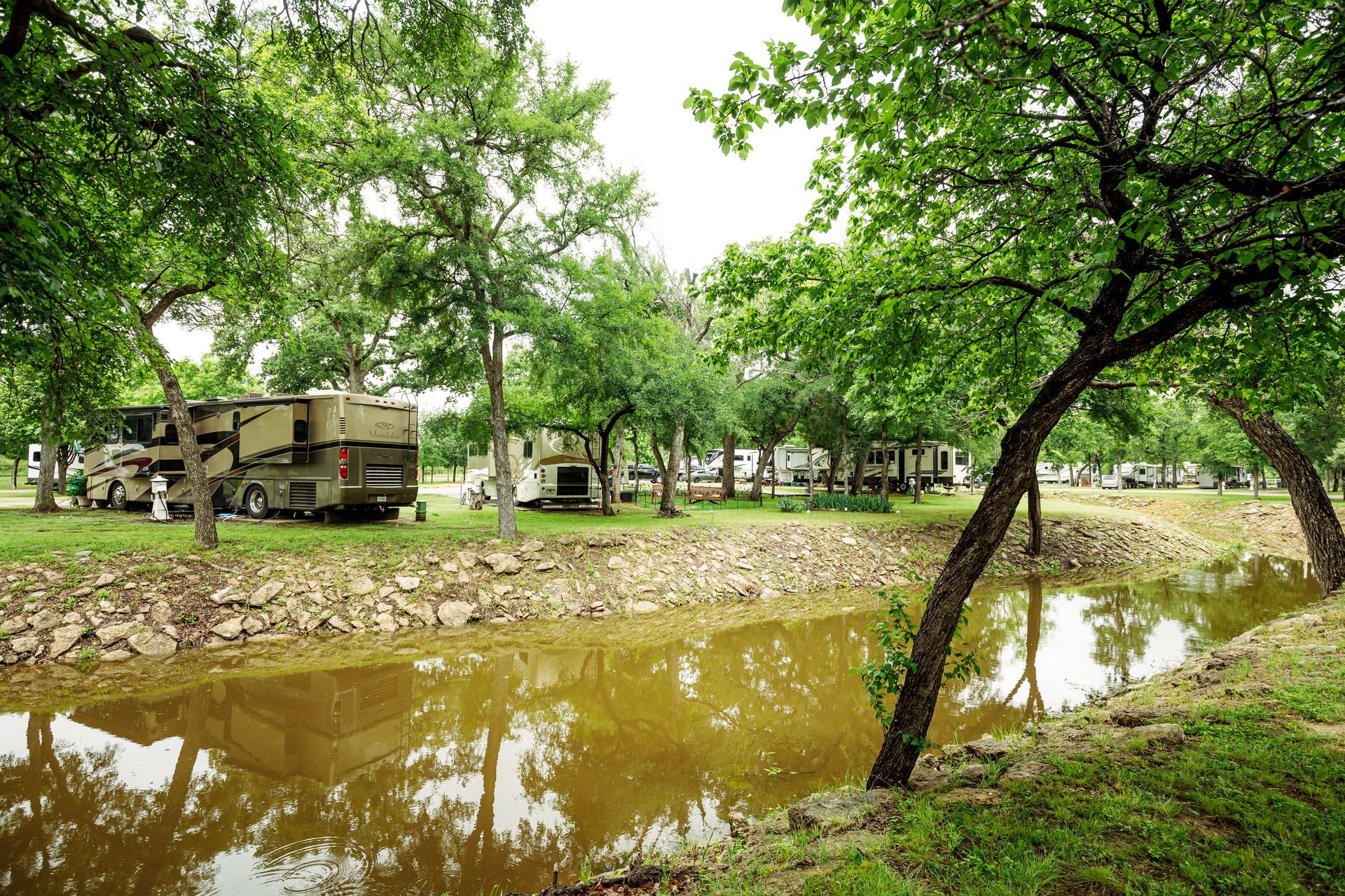 A couple of rvs parked next to a river surrounded by trees.