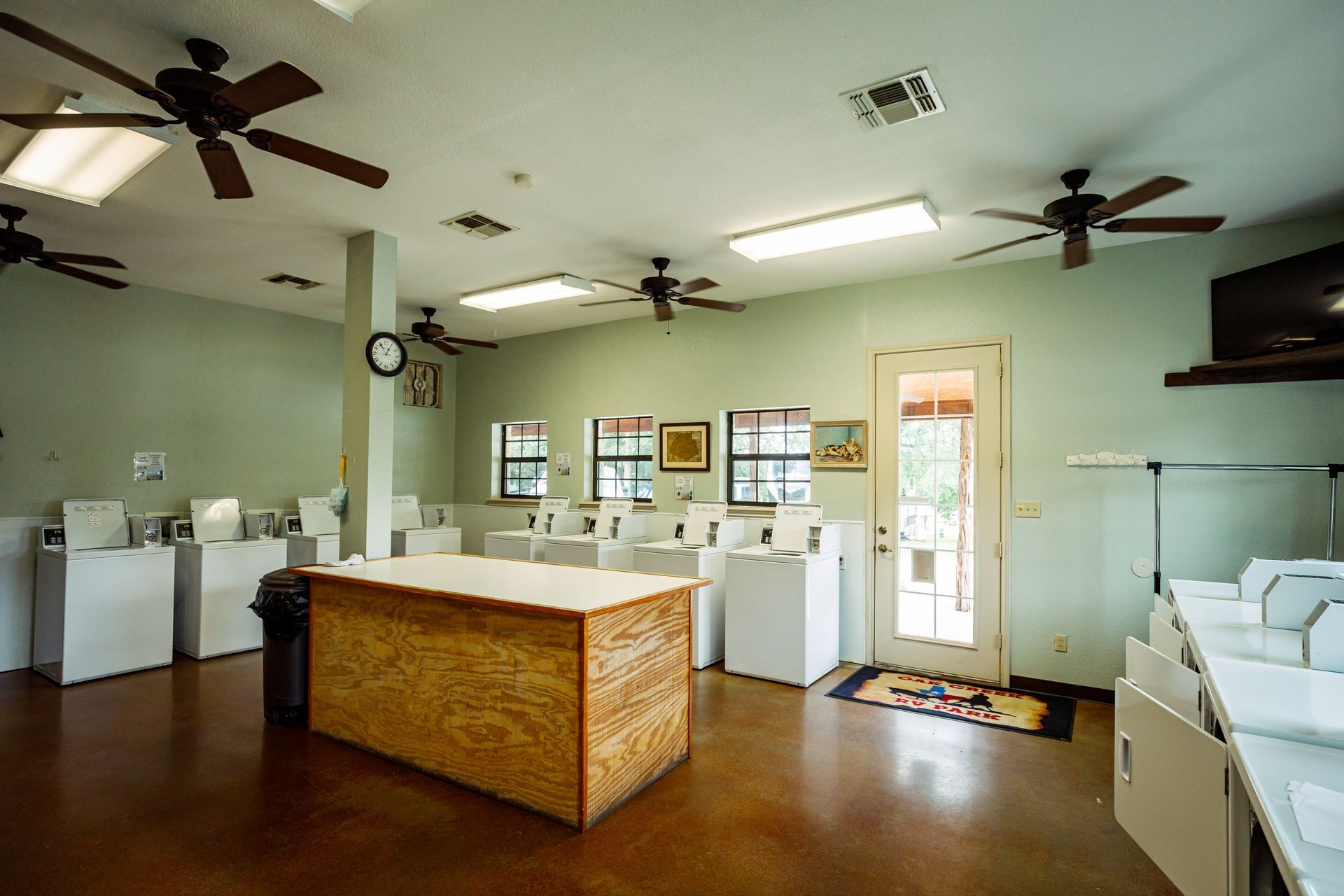 A laundromat with lots of washers and dryers and a ceiling fan.