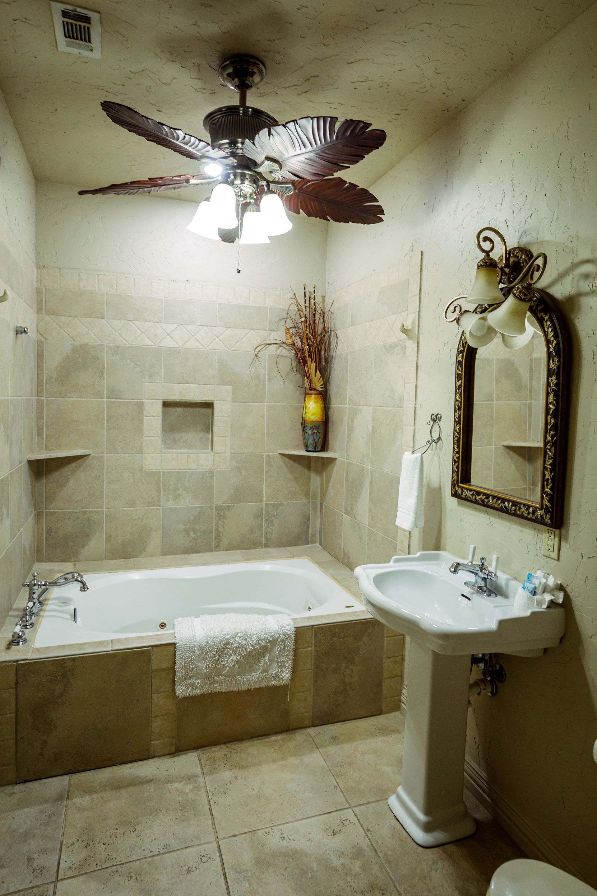 A bathroom with a jacuzzi tub , sink , mirror and ceiling fan.