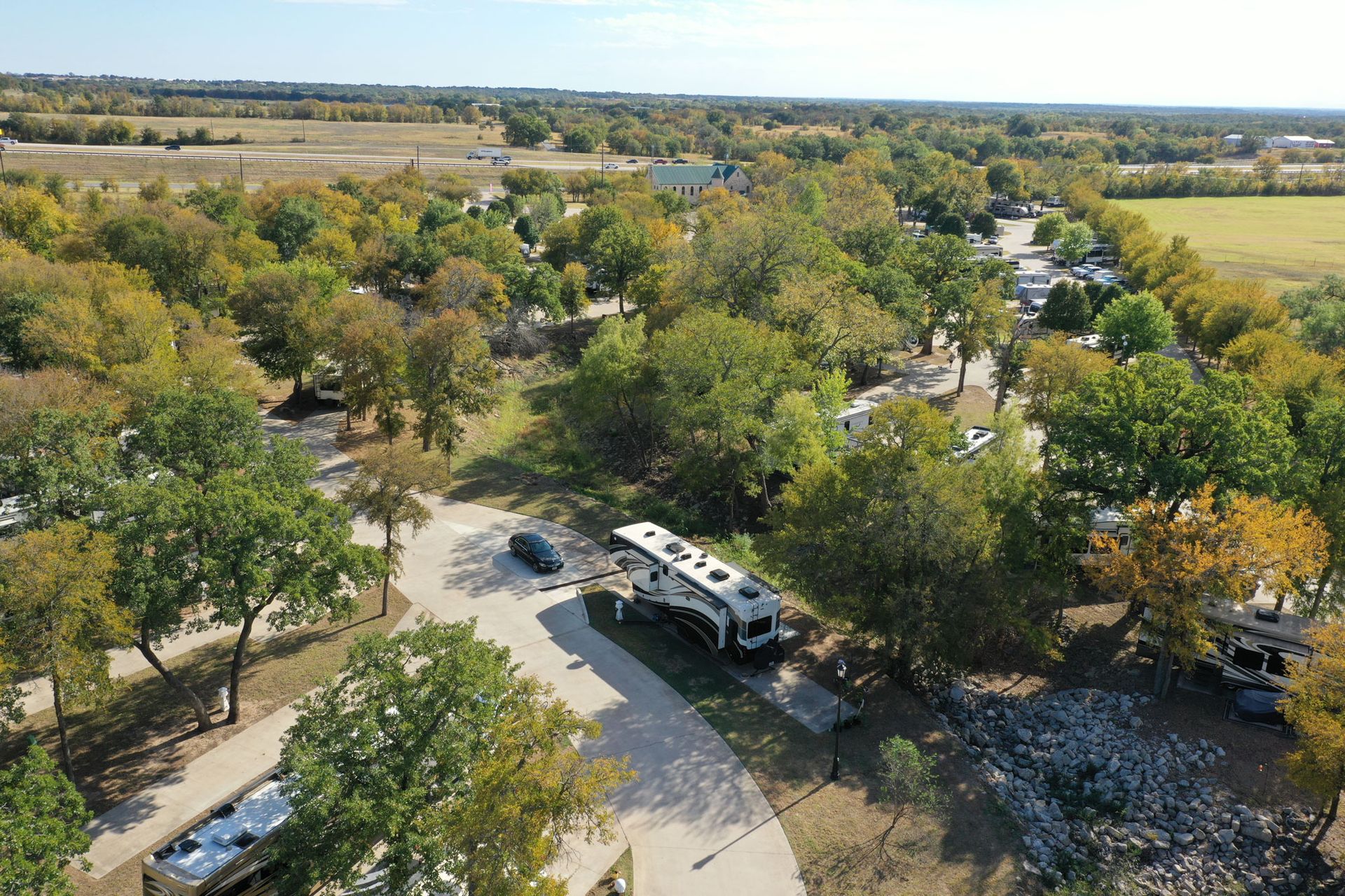 An aerial view of a rv park surrounded by trees and a road.