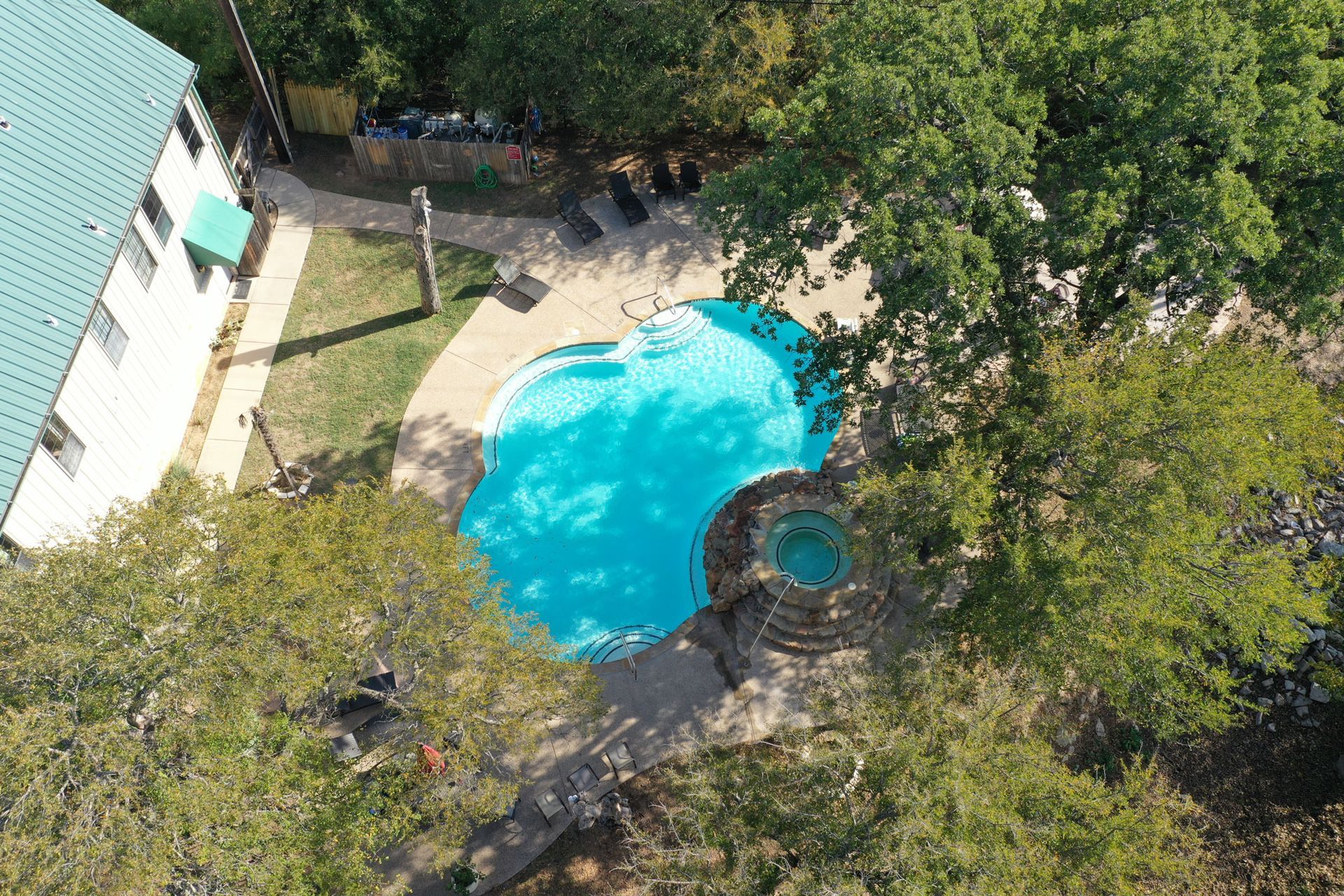An aerial view of a swimming pool surrounded by trees and a house.