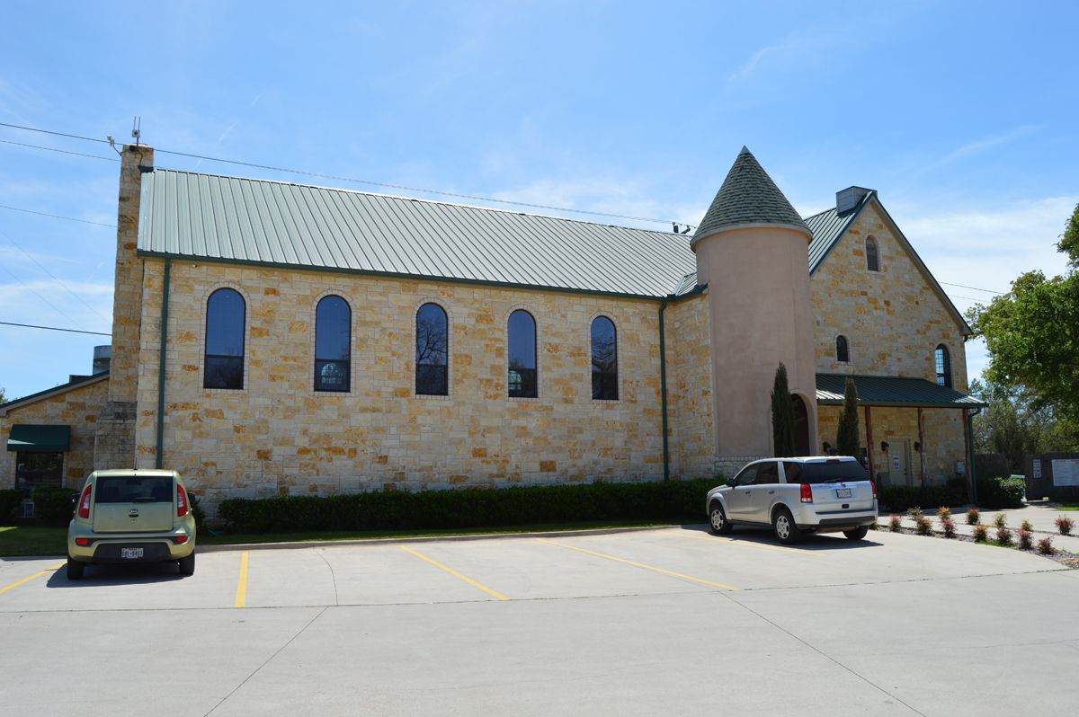A church with cars parked in front of it on a sunny day.