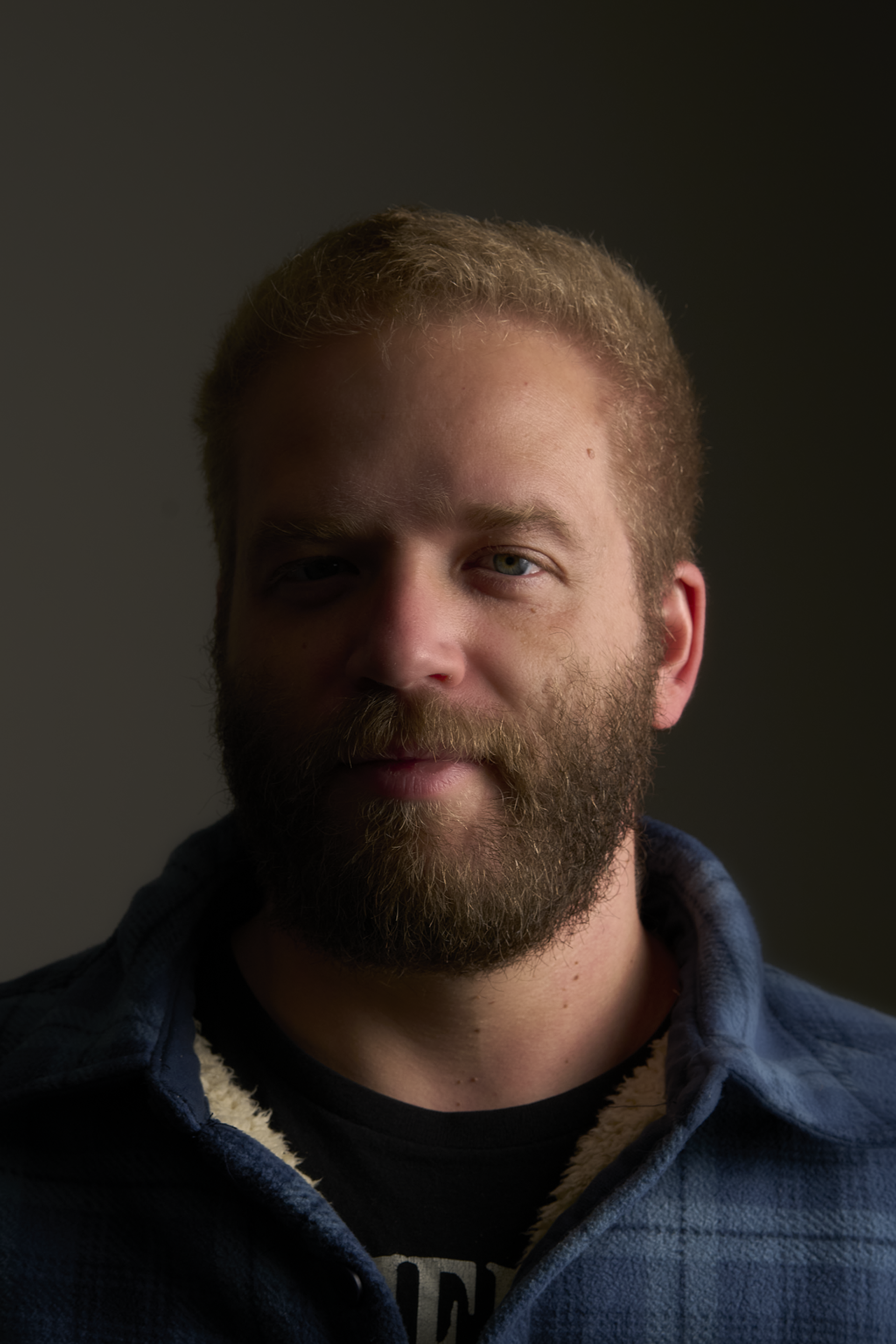A man with a beard is wearing a blue plaid shirt.