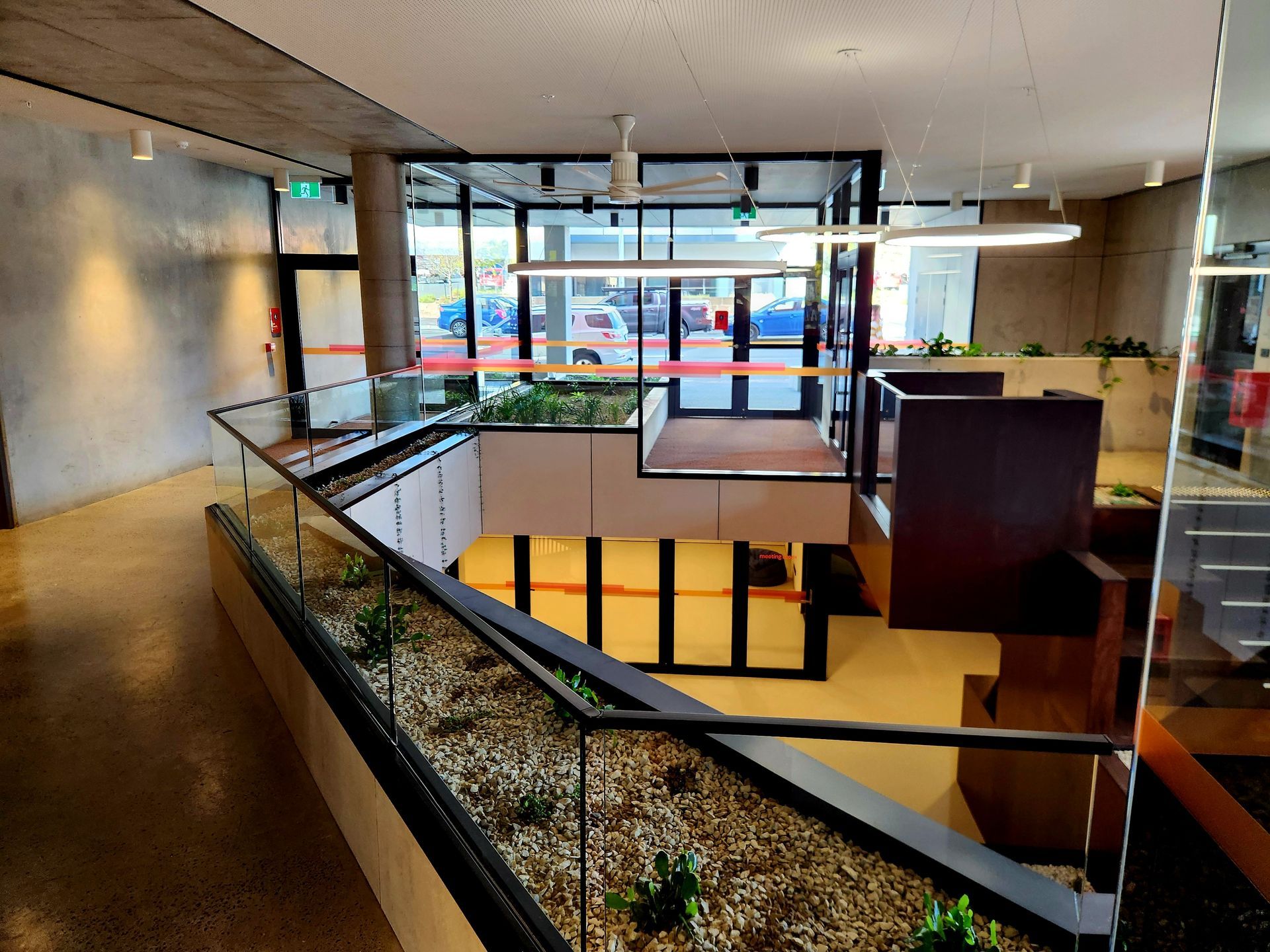 Interior view of a modern building with a raised platform, glass railings, and plants.