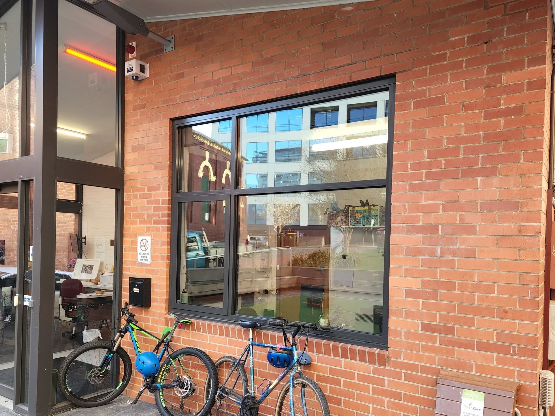 Brick building exterior with large window reflecting city, bikes parked below.