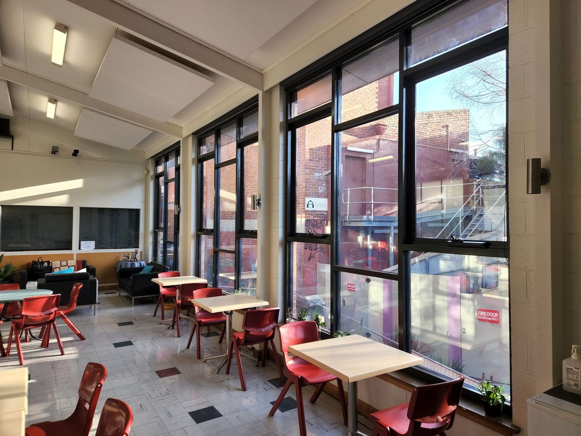 Cafeteria with red chairs, small tables, large windows looking out onto a brick building.