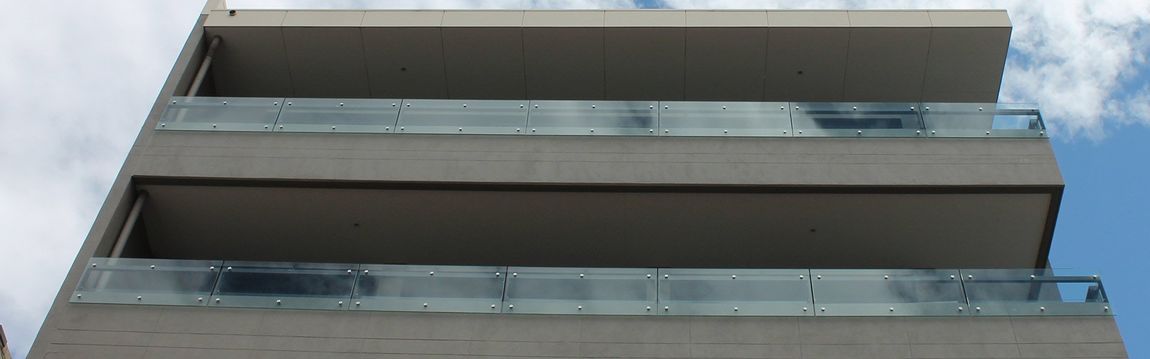 Building exterior with balconies. Glass railings. Cloudy sky.