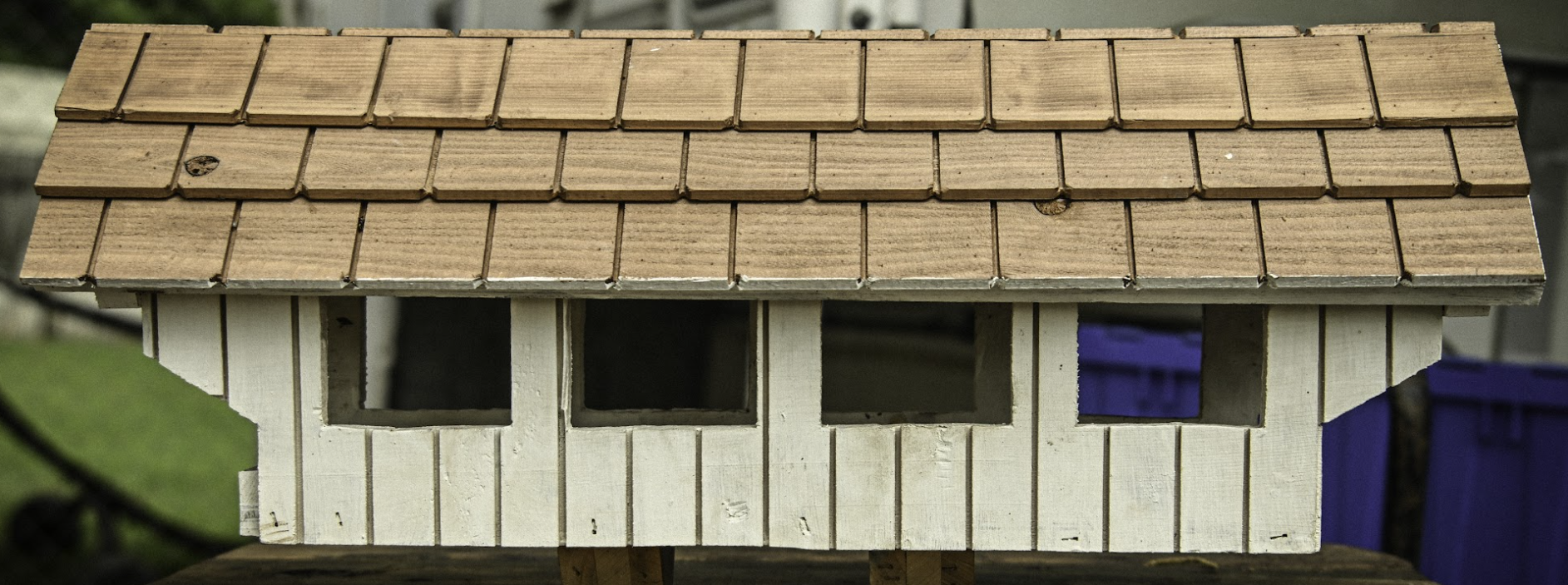 Small white shed with a tan shingled roof and a purple door, viewed from the front.