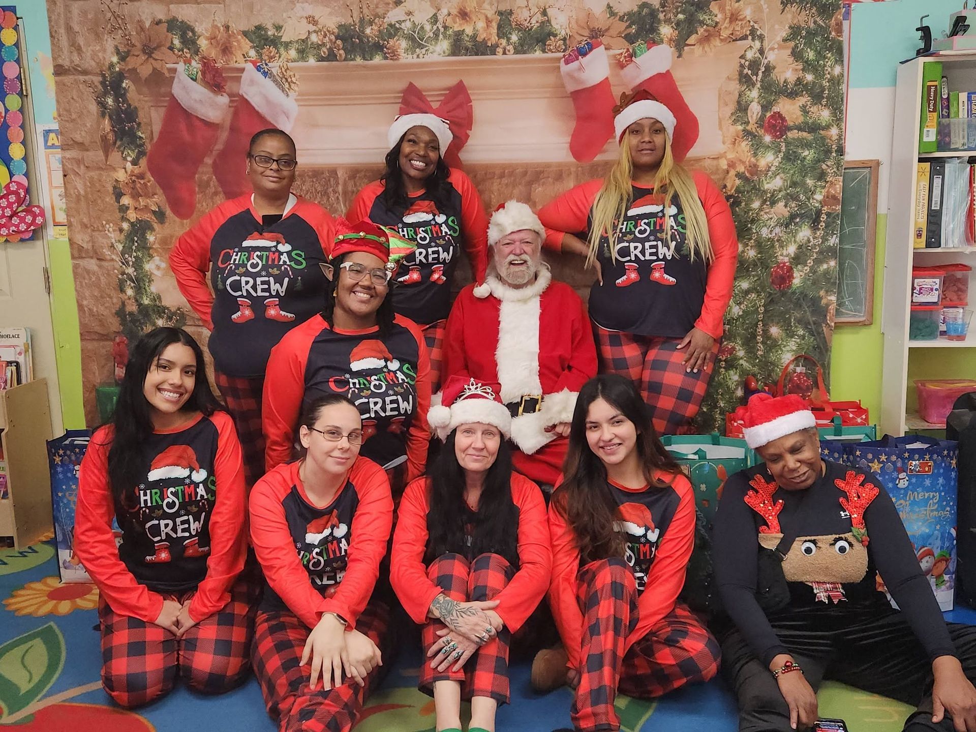 Santa with a group in red-and-black holiday pajamas posed in front of a festive fireplace backdrop
