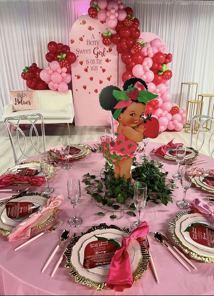 A table set for a strawberry themed birthday party with plates , utensils , and balloons.