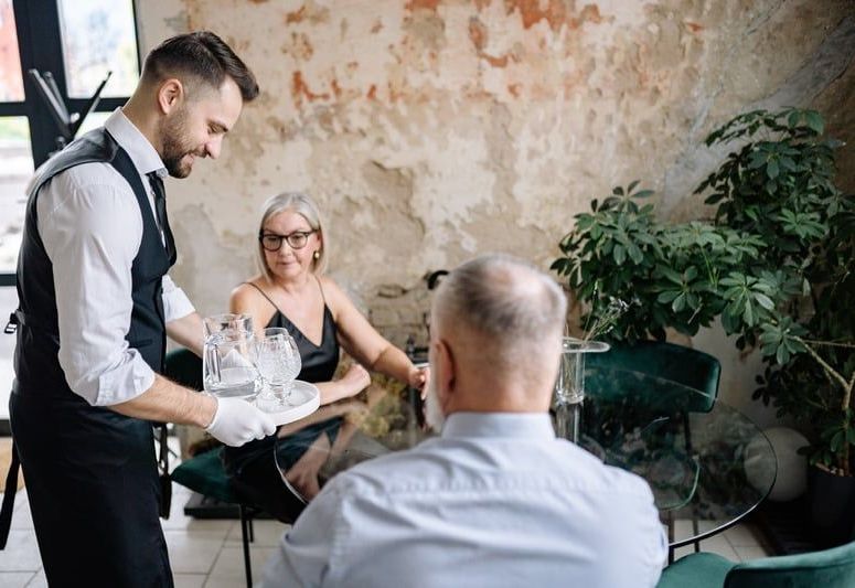 A waiter is serving a glass of water to a woman and a man in a restaurant.